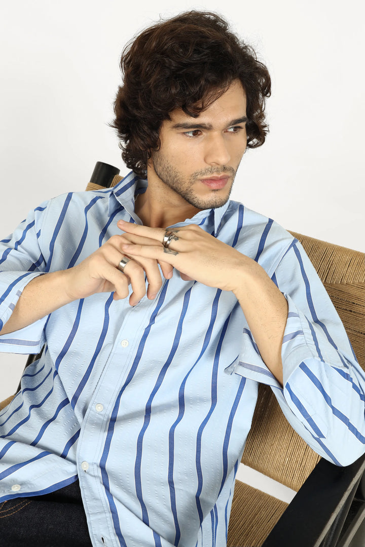 Man wearing a light blue striped shirt sitting on a chair.