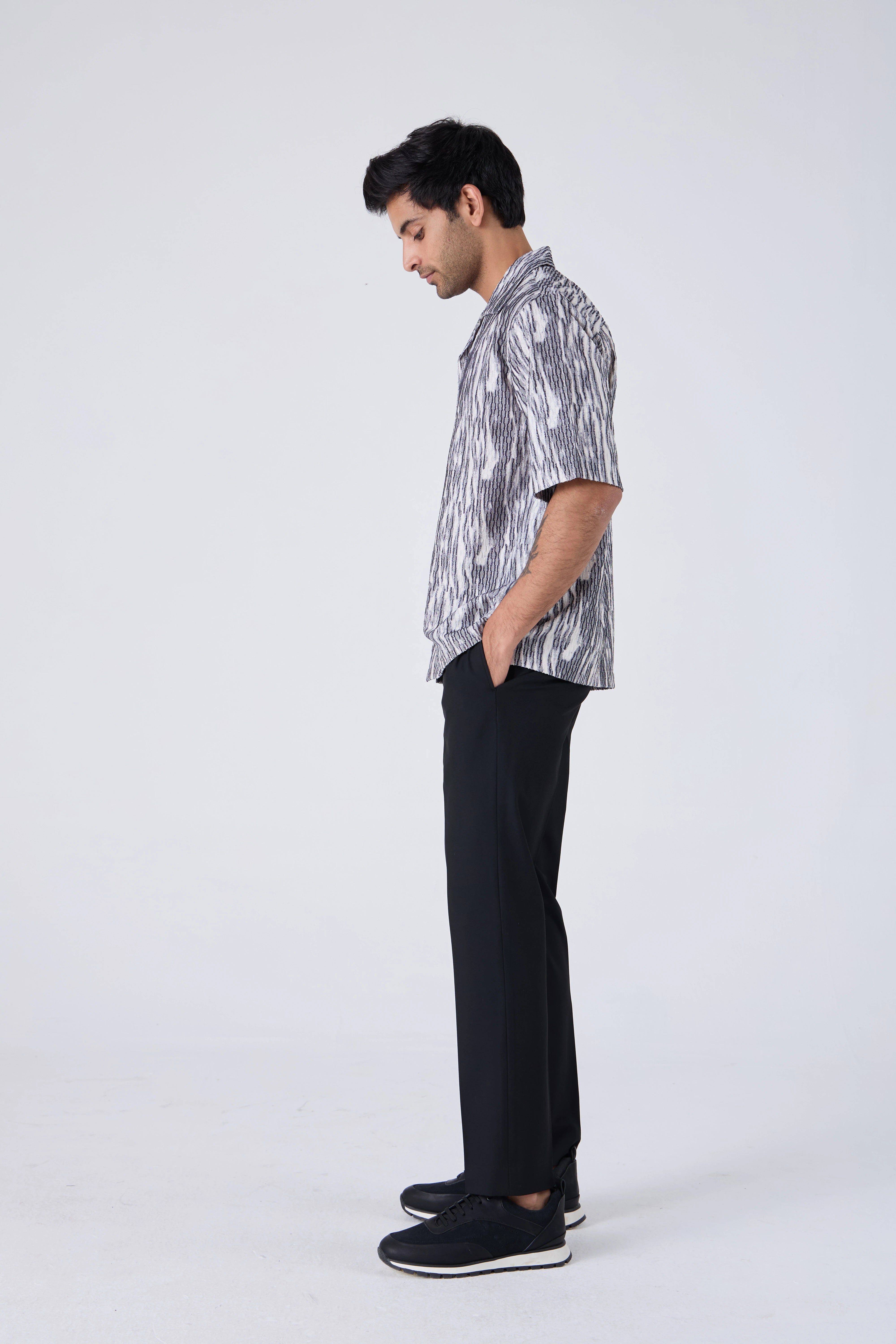 Man wearing a patterned shirt and black pants on a white background