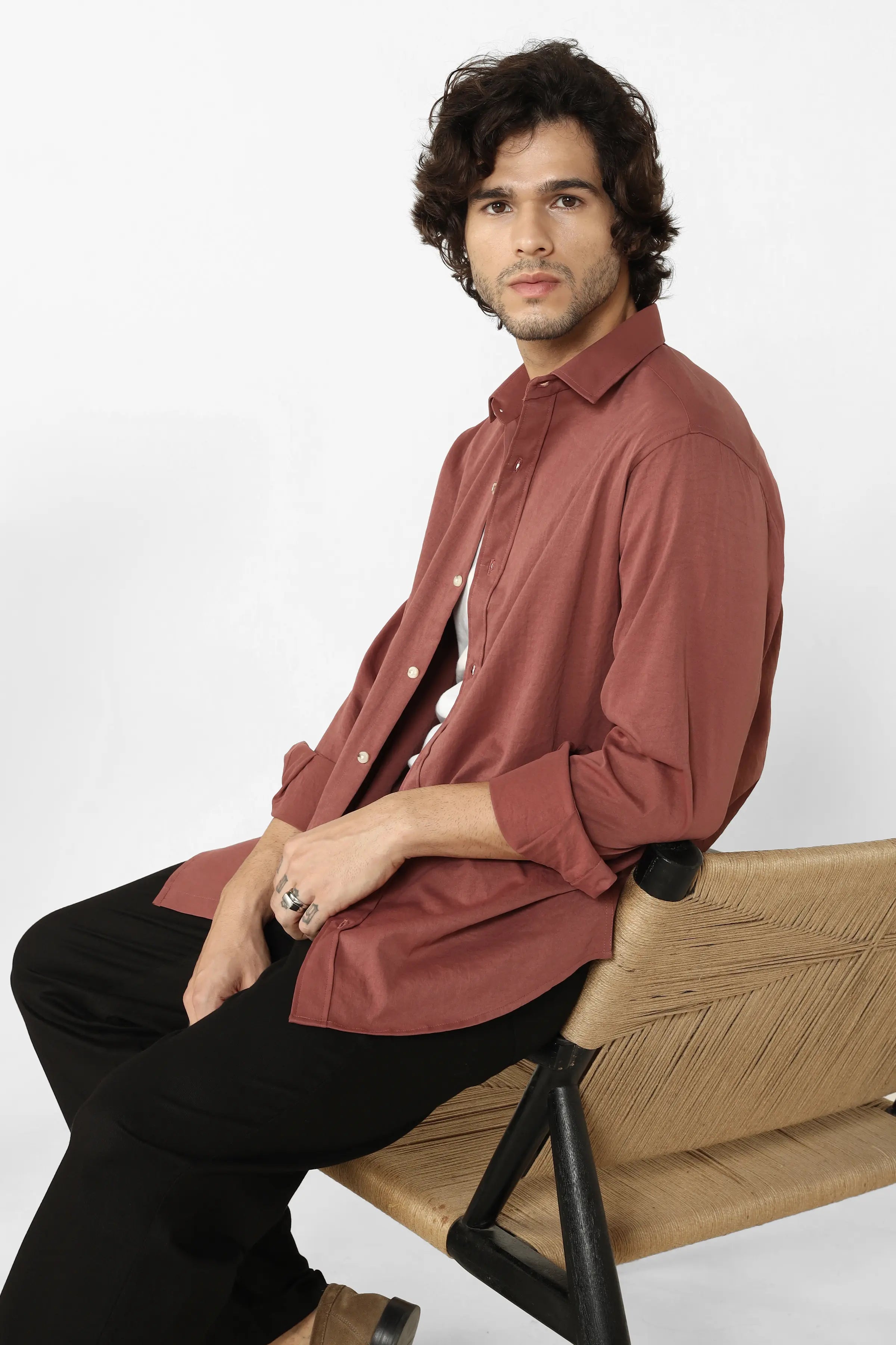 Man wearing a Rust Creased Cotton Shirt sitting on a wooden chair against a white background
