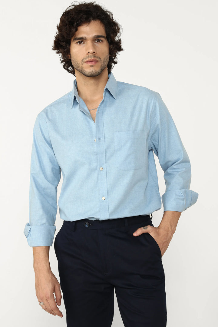 Man wearing a light blue oxford shirt and dark pants on a white background