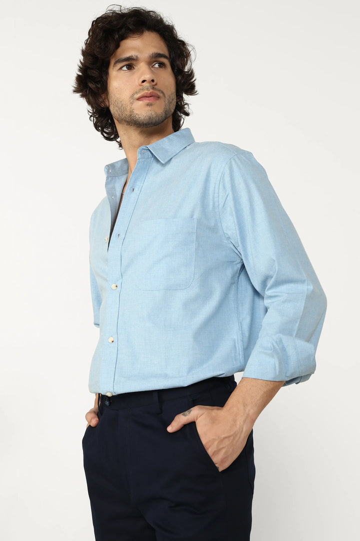 Man wearing a light oxford blue shirt and dark pants on a white background