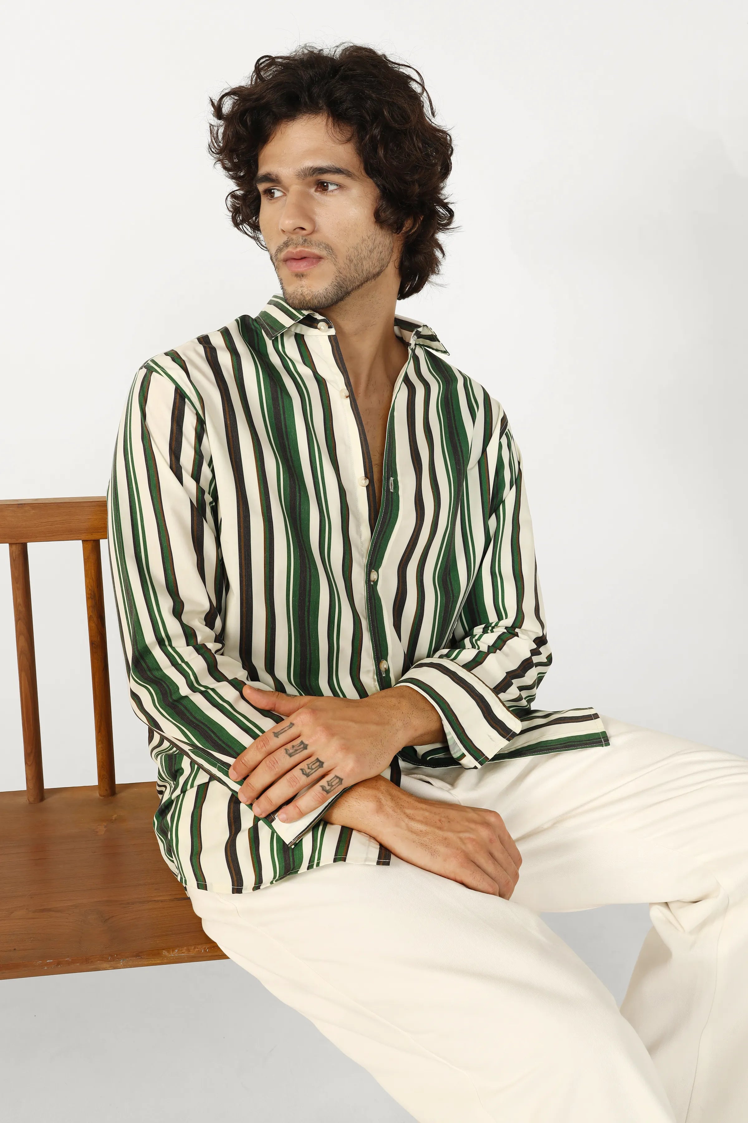 Man wearing a green and white striped shirt sitting on a wooden chair.