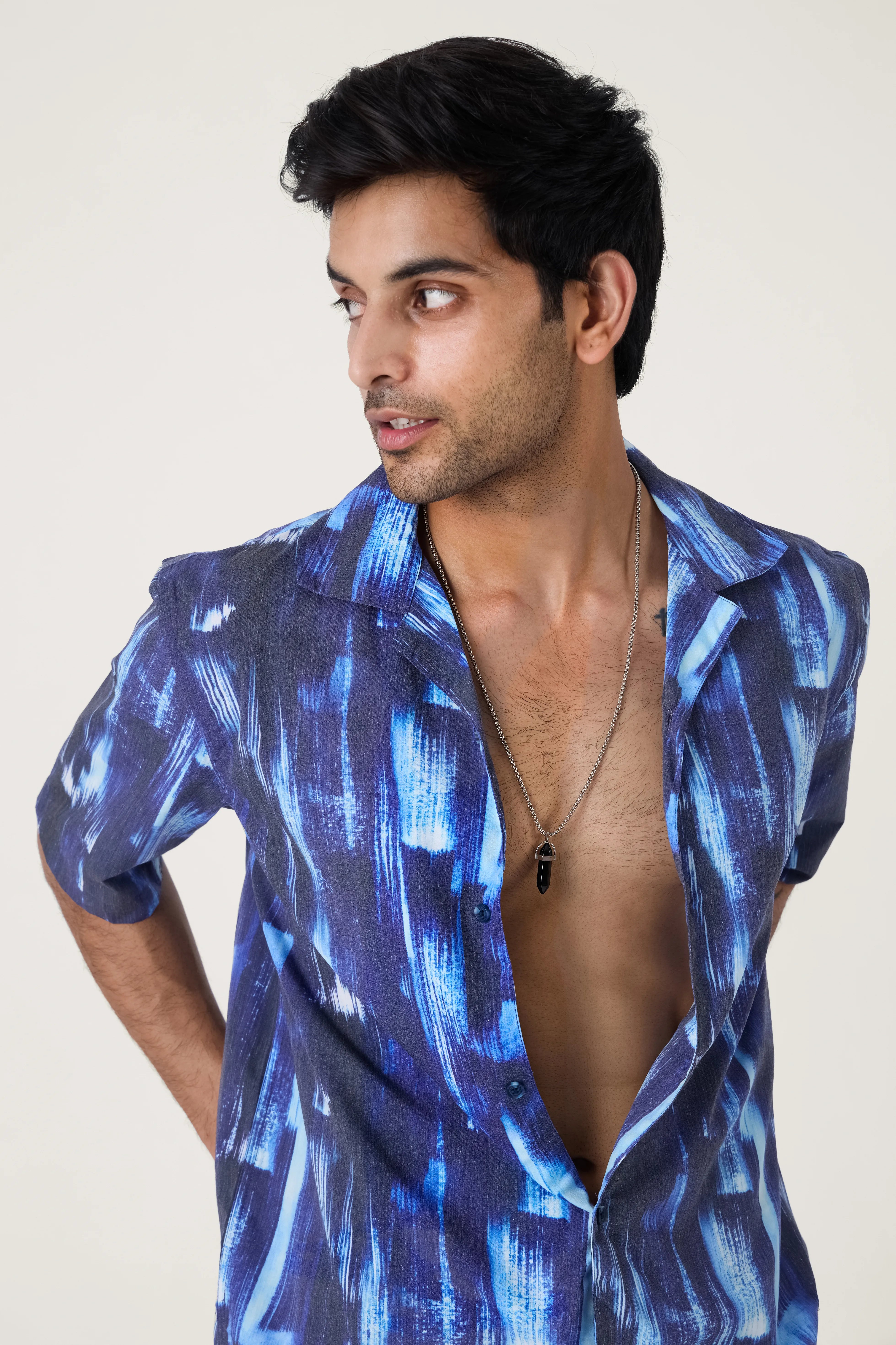 Man wearing a blue patterned shirt with open front on a plain background.
