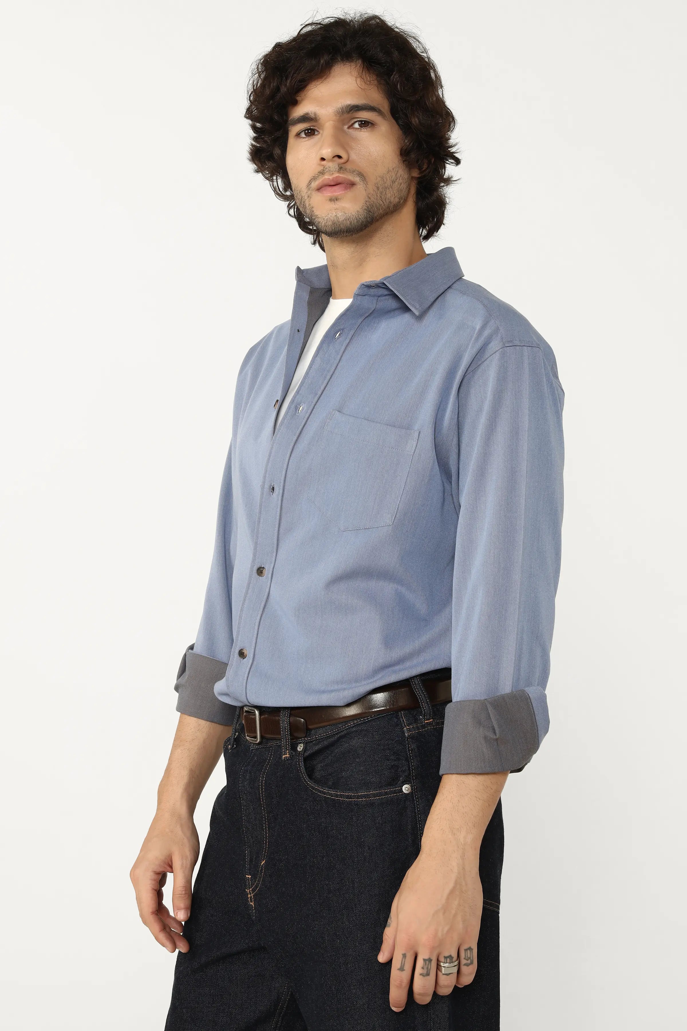 Man wearing a Oxford Cotton Twill Shirt with rolled-up sleeves and dark jeans on a white background