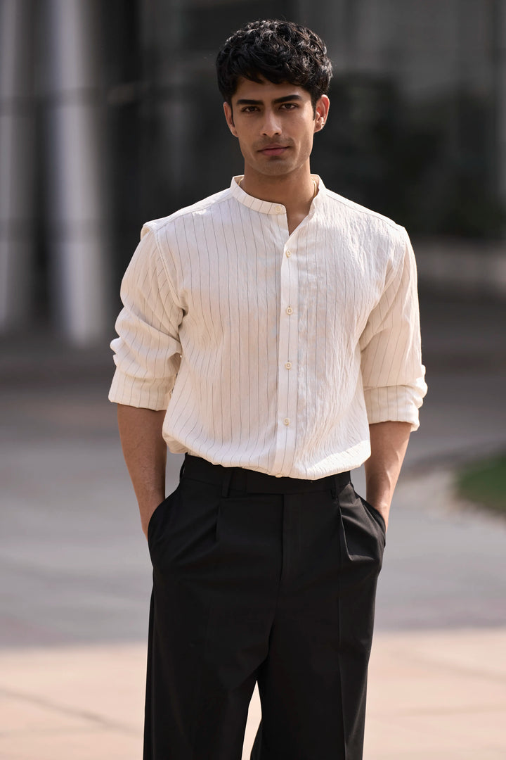 Man wearing a white flowing stripe button-up shirt and black pants standing outdoors.