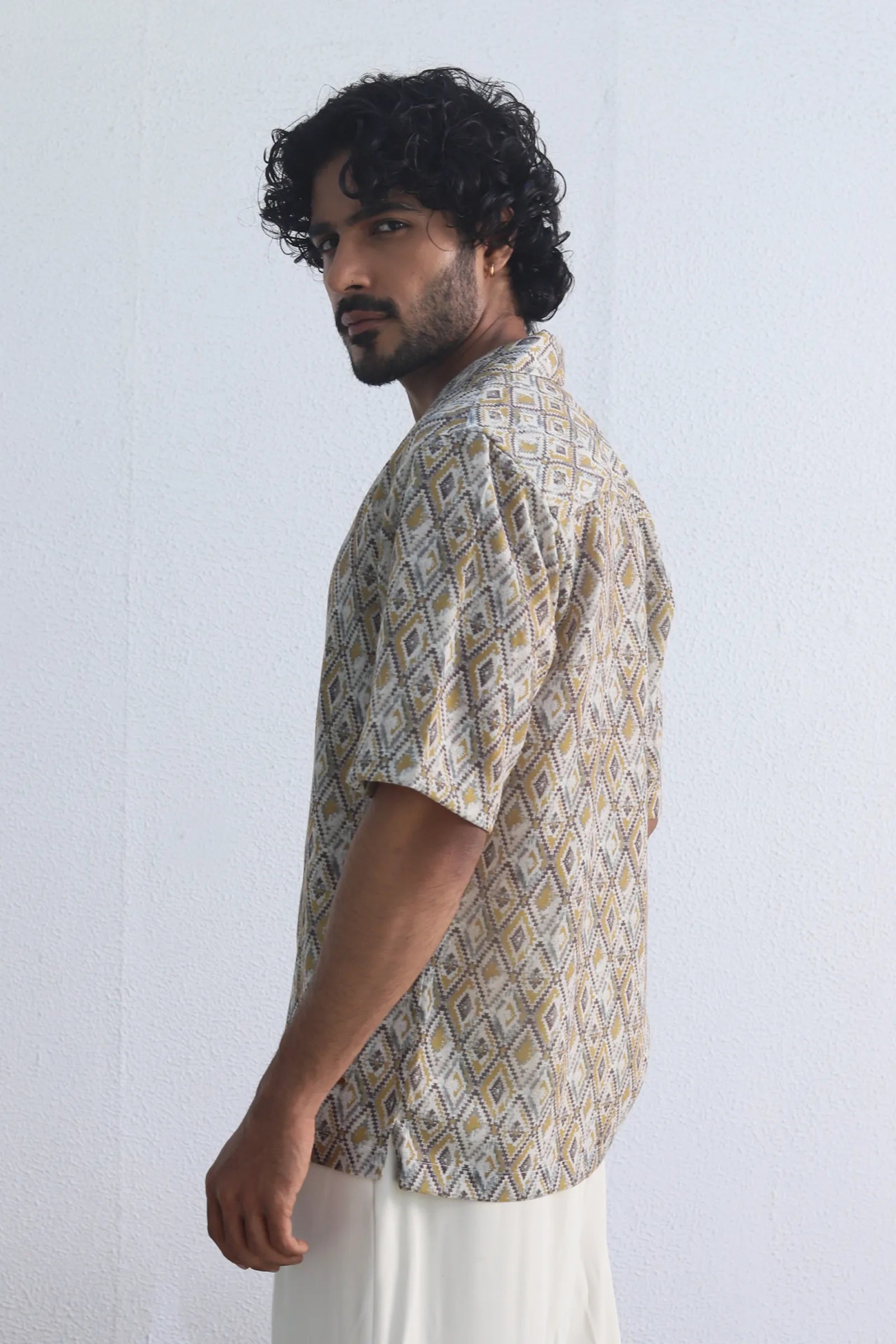 Man wearing a Yellow Harlequin Printed Shirt and white pants against a light background