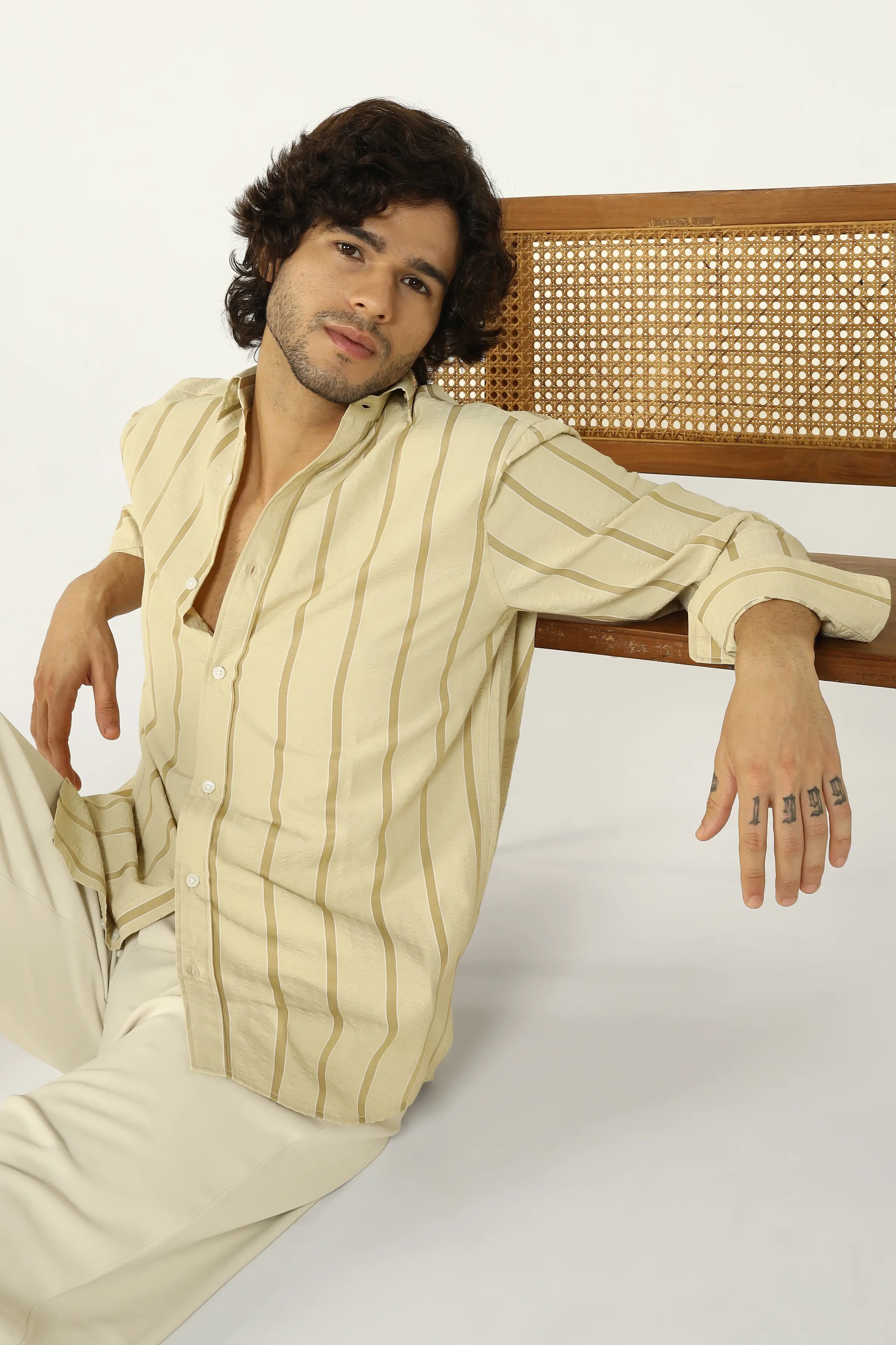 Man wearing a Yellow Seersucker striped shirt and pants sitting on a wooden bench.